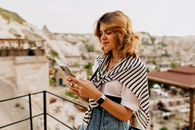 Eski Avrupa şehrinin arka planında akıllı telefon kullanarak beyaz tişört ve soyunmuş tişört giyen akıllı Avrupalı kadın portresi. Yüksek kalite fotoğraf
