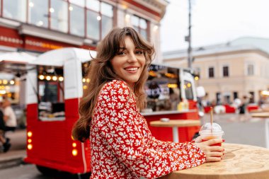 Parlak yaz kıyafetiyle gülümseyen güzel kız kameraya poz veriyor ve ılık yaz akşamında dışarıda dinleniyor. Yüksek kalite fotoğraf