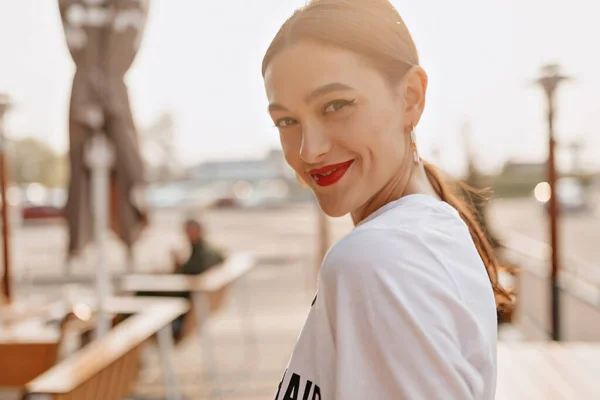 Di luar potret gadis cantik yang menarik dengan bibir merah menatap kamera dan tersenyum di bawah sinar matahari di kota musim panas — Stok Foto