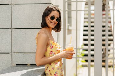 Caddede gülümseyen neşeli bayan. Parlak yaz elbisesi içindeki zarif esmer kız fotoğraf çekerken şaka yapıyor..