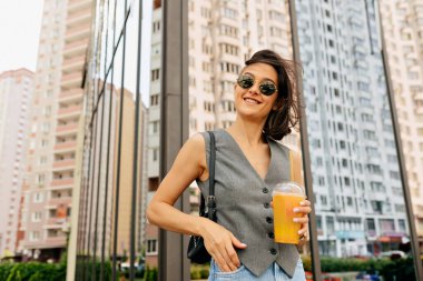 Parlak bayan güneşin tadını çıkarıyor, yüksek binanın arka planındaki kameraya bakıyor. Neşeli eğlence ve unutulmaz yaz günü deneyimi.