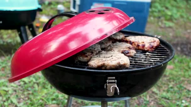 Cooking meat on red round barbecue grill bbq rotating beaf steaks with open fire smoke. Outside in camping — Stock Video