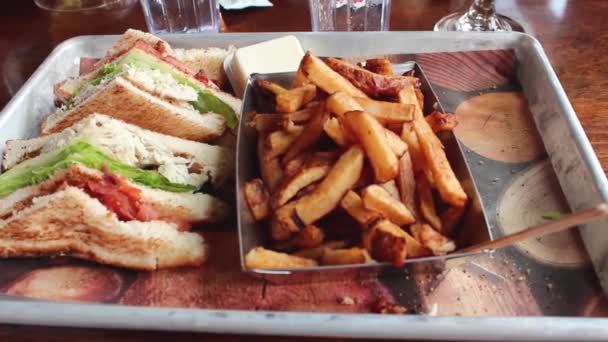 Clubsandwich met kippenvlees, frietjes op een bord met mosterd en ketchup. Clubsandwich op een wit bord met gesneden toast brood, mayonaise tomaten, sla, kaas en spek. — Stockvideo