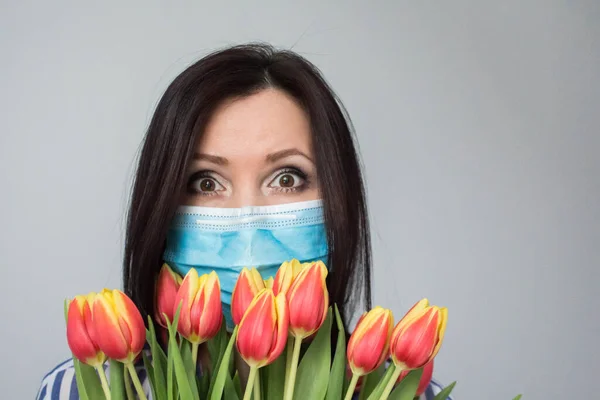 Smiling woman doctor nurse with protective medical mask, with bouquet of tulip flowers, gift, celebration, medical worker day. Mothers day. Light grey background, copy space