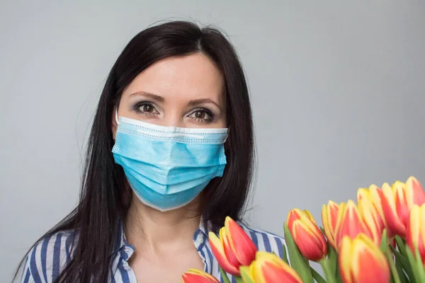 Smiling woman doctor nurse with protective medical mask, with bouquet of tulip flowers, gift, celebration, medical worker day. Mothers day. Light grey background, copy space