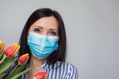 Koruyucu tıbbi maskeli gülümseyen kadın hemşire, bir buket lale çiçeği, hediye, kutlama, sağlık çalışanları günü. Anneler Günü. Açık gri arkaplan, boşluğu kopyala