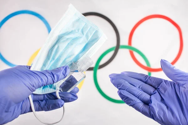 Tıbbi maskeli tıbbi teknisyen ve sporcular için dezenfektan ve arka planda Olimpiyat yüzüklü bayrak. Aşı için bağışıklık