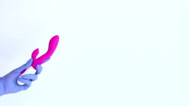 Plastik eldivenli bir kadının elinde pembe bir vibratör var. Modern tasarımlı bir seks oyuncağı.