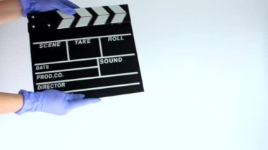 Tıbbi lastik eldivenli eller beyaz arka planda film yapım alçıpan tutuyor..