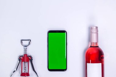 Gül ve beyaz masa üzerinde tirbuşon ile. Model telefon. Yeşil ekran. Kopyalama alanı olan üst görünüm. Mesaj için yer var. Şarap şişesi boyunları.