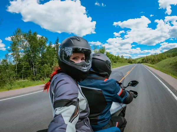 Motosiklet yolcusu kasklı genç bir kadın boş bir arazide motosiklet sürerken aksiyon kamerasında selfie çekiyor..