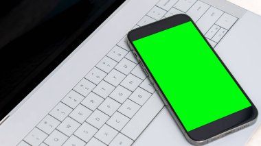 Smartphone, dijital tasarım kavramları ve yaratıcılığı sergilemek için ideal, şık bir dizüstü bilgisayarın klavyesine yerleştirilmiş canlı yeşil bir ekran sunar.