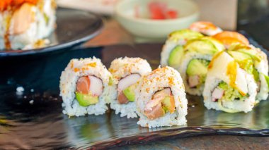 Colorful sushi rolls displayed on a black plate, featuring fresh ingredients and artistic arrangement, ideal for food photography and culinary art