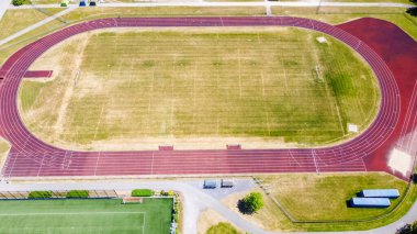 Kırmızı şeritler ve çimenli alanların yer aldığı koşu pistinin hava perspektifi, açık bir spor sahası ve atletik kullanım için yakınlardaki bir manzarayı vurguluyor