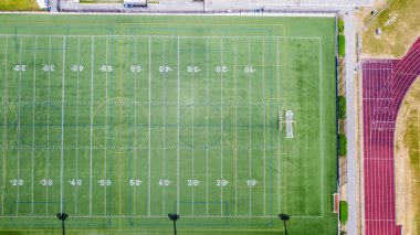 Aerial perspective of a sports field with clear yard lines and goalposts, surrounded by a running track, highlighting the vibrant green turf and structure