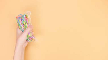 Bir el, parlak turuncu arka planda parlak lastik bantlarla dolu plastik bir çanta tutar. Bu eğlenceli görüntü zanaat, moda ya da okul malzemesi temalarına uyuyor, yaratıcılık sergileniyor.