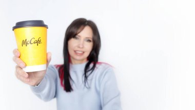 Ottawa On Canada - 2024-10-28: Uzun siyah saçlı neşeli kadın beyaz arka planda neşeli bir şekilde McDonalds sarı kahve fincanını tutuyor.