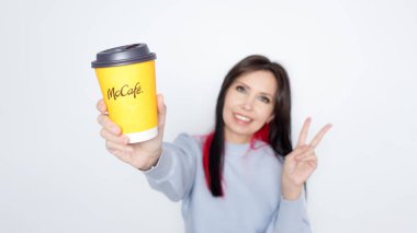 Ottawa On Canada - 2024-10-28: Uzun siyah saçlı neşeli kadın beyaz arka planda neşeli bir şekilde McDonalds sarı kahve fincanını tutuyor.