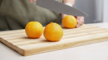 Masadaki kesme tahtasının üzerinde portakal renginde mandalina kesen eller, yemek yapmak için bir sürü sulu taze meyve..