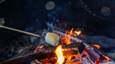 Çubuğun üzerindeki lokum bir kamp ateşinde kavruluyor, parlayan közler ve alevler açık havada sıcaklık ve ortam sağlıyor.