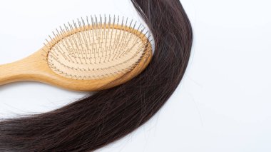 Beyaz bir yüzeyde parlak koyu renk saçların yanına yerleştirilmiş ahşap saç fırçası saç bakımının ve bakımının sağlıklı kilitler için önemini vurguluyor.