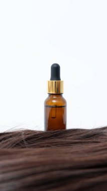 Siyah şapkalı kehribar şişesi lüks kahverengi saçlara dayanır. Saç ve bakım için tasarlanmış bir güzellik ürününün altını çizer.