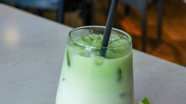 Iced green tea drink in a transparent glass filled with ice cubes and a black straw, ideal for warm weather and social occasions