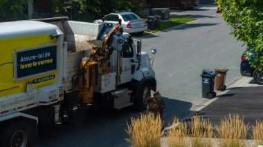 Gatineau QC, Kanada - 10 Eylül 2025: Quebec caddesindeki atık toplama aracı, çöp kutusunu kaldırmak için mekanik kolu çalıştırıyor, kentsel atık yönetimi vurguluyor