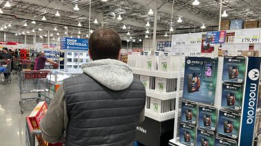 Gatineau QC, Kanada - 05 Aralık 2025: Costco 'da elektronik eşya satan adam, kalabalık bir depo atmosferinde ürün vitrinleri ve alışveriş arabaları ile