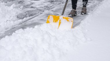 Şahıs, parlak sarı bir kürek kullanarak kaldırımdan ağır kar küreyerek kış çalışmalarını ve sakin karlı çevreyi vurguluyor.