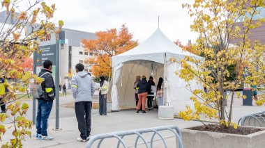 Ottawa ON, Kanada - 25 Ekim 2025: uOttawa Üniversitesi Açık Kapılar etkinliği katılımcıların renkli sonbahar ağaçları ve çağdaş mimarinin ortasındaki beyaz bir çadırda etkileşimlerine yer veriyor.