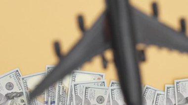 Model uçak, seyahat ve zenginlik hayallerini sembolize eden, renkli bir zemin ve görsel cazibeyi artıran, nakit para banknotlarının üzerinde süzülür.