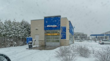 Gatineau QC, Kanada - 30 Kasım 2025: Fırtınada karla kaplı zemin ve ağaçlarla çevrili mavi giriş işaretli bir araba yıkama binasının yer aldığı karlı bir sahne