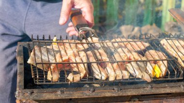 Taze balık ve sebzeler mangalda kızartılıyor, dumanlar yükseliyor ve parlak renkler, açık havada yemek pişirme atmosferi yaratıyor.