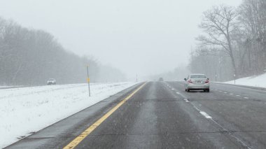 Syracuse NY, ABD - 18 Şubat 2025: Karlı bir otoyolda ilerleyen araçlar, bulanık ağaçlar ve düşük hava koşullarında görüş mesafesi