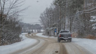 Gatineau QC, Kanada - 30 Kasım 2025: Yol kenarında ağaçların oluşturduğu kar fırtınası sırasında karla kaplı virajlı bir yolda giden siyah kamyonet