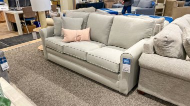 Ottawa On, Kanada - 04 Ocak 2026: Dekoratif pembe yastıklı açık gri kumaş kanepe bir mobilya galerisinde sergilenmektedir, arka planda çeşitli oturma seçenekleri ve ev dekorasyonu ürünleri görülebilir