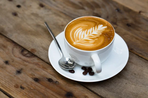 Kopje warme latte art koffie op houten tafel — Stockfoto