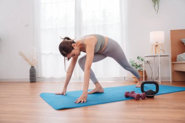 Asyalı bir kadın yoga minderinde ağırlık çalışıyor. Dambıl ve kettlebell ile. Esnekliği, gücü ve sağlıklı yaşam tarzını geliştirmek için dinamik egzersiz yapıyor..