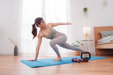 Asyalı bir kadın yoga minderinde ağırlık çalışıyor. Dambıl ve kettlebell ile. Esnekliği, gücü ve sağlıklı yaşam tarzını geliştirmek için dinamik egzersiz yapıyor..