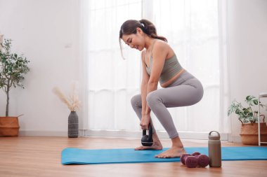 Evde yoga minderinde Asyalı bir kadının kettlebell egzersizi, kuvvet eğitimi, düşük vücut egzersizi ve en az spor ekipmanıyla kadın fitness rutini..