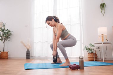 Evde yoga minderinde Asyalı bir kadının kettlebell egzersizi, kuvvet eğitimi, düşük vücut egzersizi ve en az spor ekipmanıyla kadın fitness rutini..