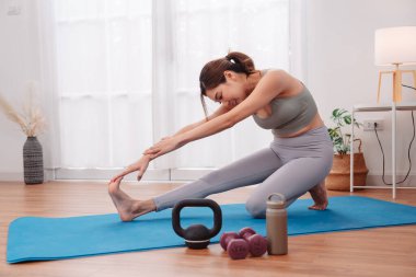 Evde yoga minderinde Asyalı bir kadınla egzersiz yapmak, ısınma rutini, kettlebell, dambıl ve spor salonu ve hareketlilik eğitimi için su şişesi..