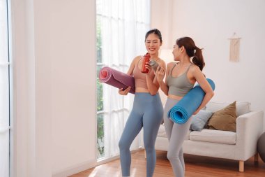Yoga, fitness, wellness, stretching, workout, healthy lifestyle, self care, activewear, training, home exercise, two young Asian women walking after yoga class, holding mats and bottles.