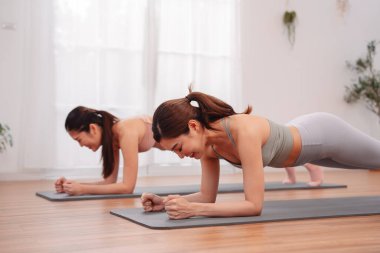 Asyalı kadınlar evlerinde yoga minderleri üzerinde birlikte poz veriyorlar. İç egzersizlerde temel dayanıklılık ve zindelik motivasyonu geliştiriyorlar. Sağlıklı yaşam tarzını ve vücut ağırlığı eğitimini destekliyorlar..
