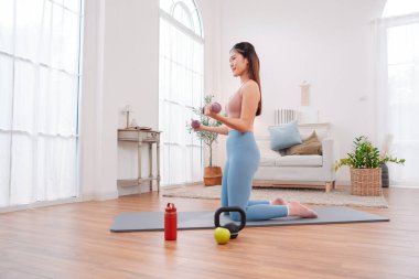 Evde egzersiz yapan Asyalı kadın, huzurlu bir oturma odası ortamında güç, denge ve genel sağlığa odaklanıyor, aktif bir yaşam tarzı, sağlıklı alışkanlıklar ve dikkatli bir fitness eğitimi sergiliyor..