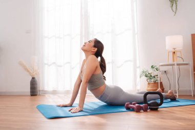 Antrenmandan sonra yatak odasında yoga minderinde uzanan bir kadın çocuk pozu veriyor. Sağlıklı yaşam tarzı, vücut iyileştirme, farkındalık ve evde esneklik eğitimi.