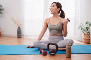 Kadın, yoga minderinin üzerinde dambıl ve kettlebell kullanarak spor yapıyor. Sağlıklı yaşam tarzı, dayanıklılık eğitimi, sağIık, spor ve iç mekanda vücut tonlaması..