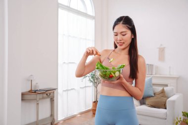 Aktif giyimli Asyalı kadın ve evde taze sebze salatası kasesi var. Temiz yeme, beslenme farkındalığı, sağlık alışkanlıkları ve dengeli bir yaşam tarzını teşvik eden ev konsepti sağlıklıdır..