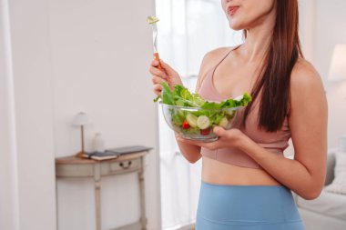 Aktif giyimli Asyalı kadın ve evde taze sebze salatası kasesi var. Temiz yeme, beslenme farkındalığı, sağlık alışkanlıkları ve dengeli bir yaşam tarzını teşvik eden ev konsepti sağlıklıdır..